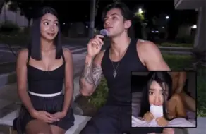 Chico tatuado con micro entrevistando a una joven latina en la calle de noche mientras ella sostiene su móvil.